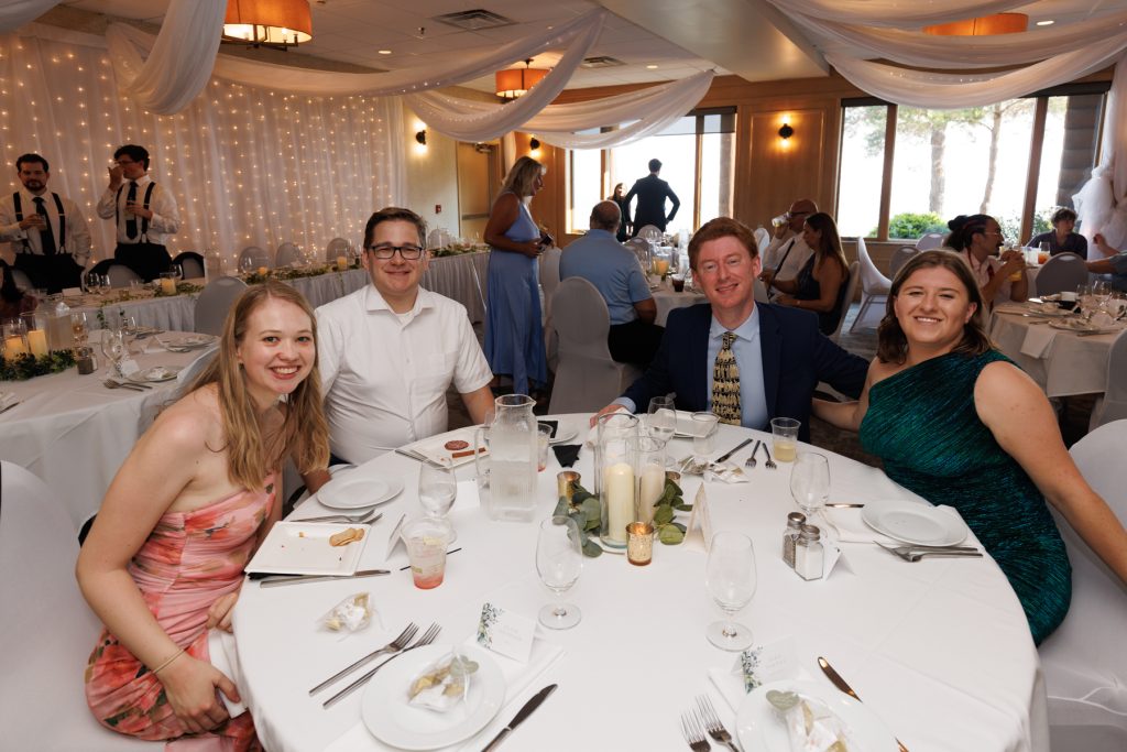 Group of wedding guests smiling and posing for a photo at a reception table