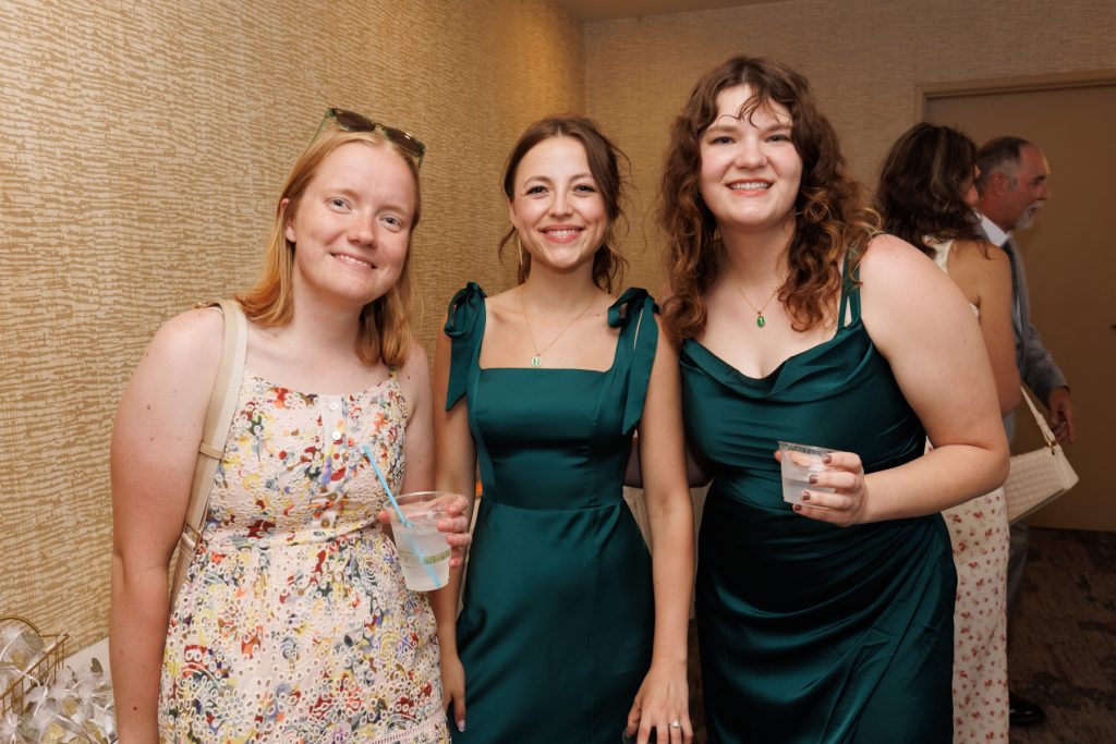 Three smiling bridesmaids in elegant dresses pose together at a Wisconsin wedding celebration, showcasing joyful