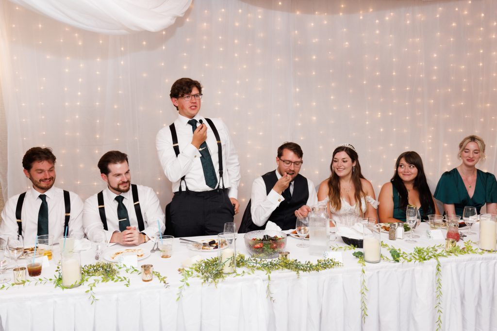 Groom giving a speech at wedding reception in Wisconsin, surrounded by wedding party and guests