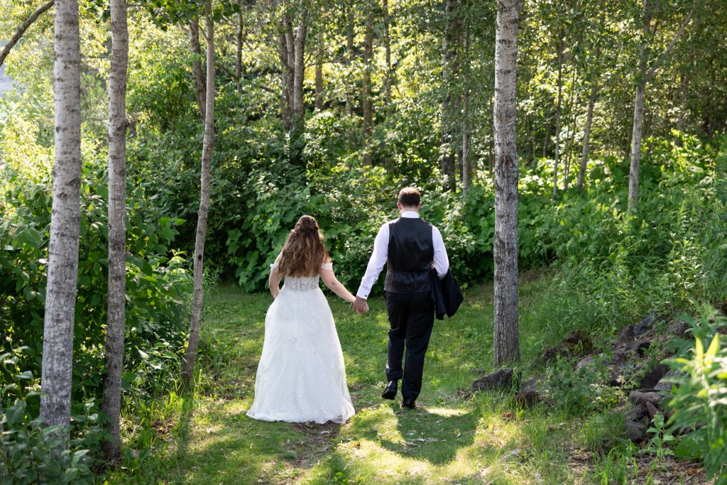 Bride in wedding dress and groom in suit walking hand-in-hand through a wooded area, showcasing