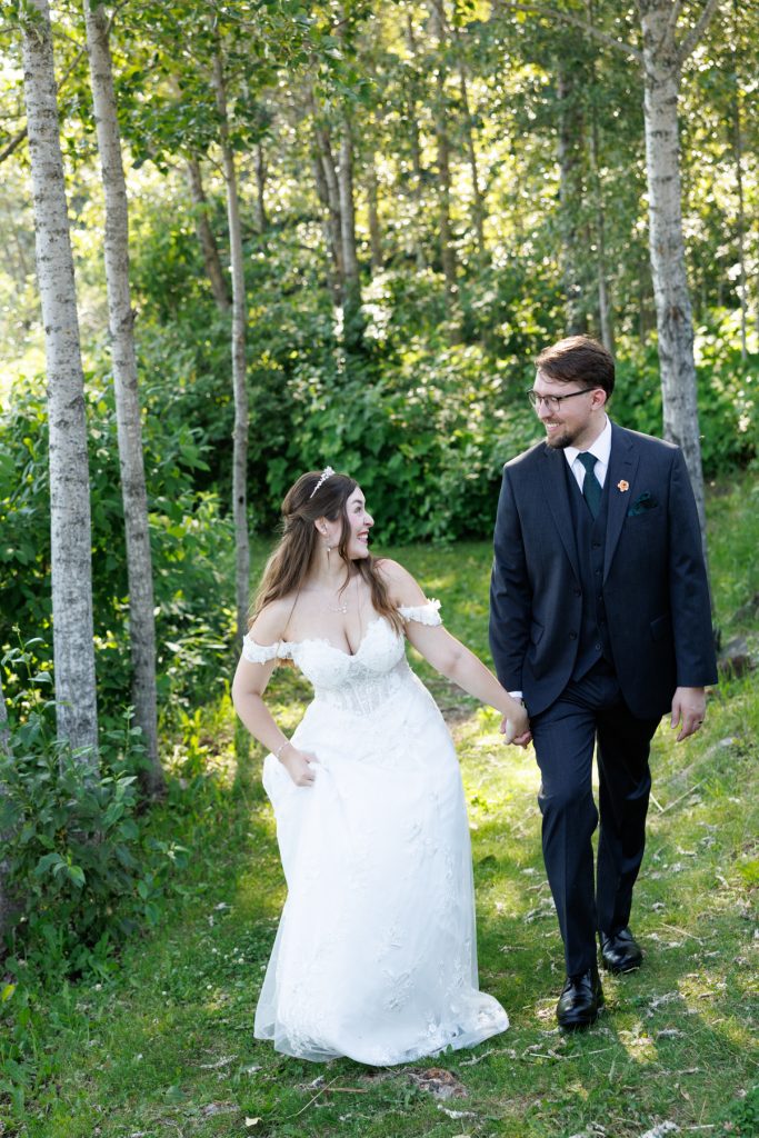Newly married couple holding hands walking through a wooded area, captured by a Wisconsin