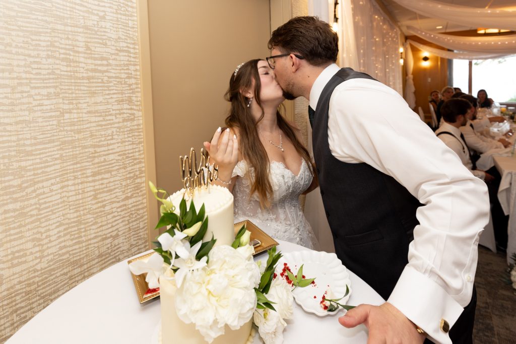 Bride and groom share a kiss while cutting their wedding cake, captured by Beau Petersen