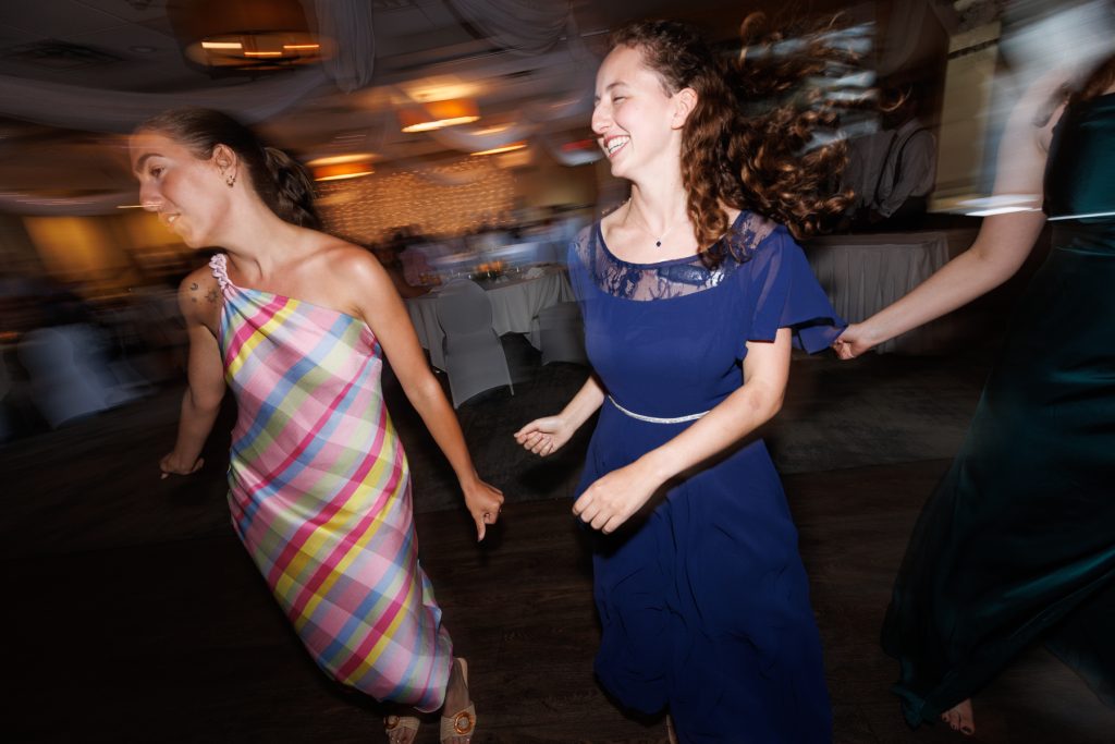 Two joyful women in dresses dancing at a wedding reception in Wisconsin, captured with motion