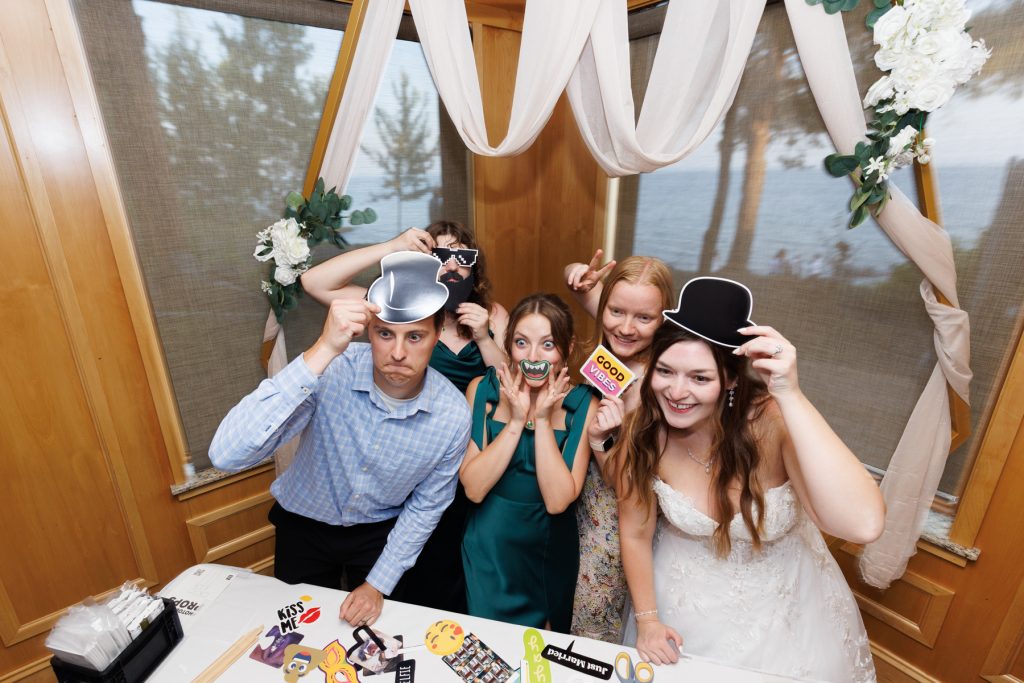 Group of wedding guests having fun in a photo booth with props overlooking a lake