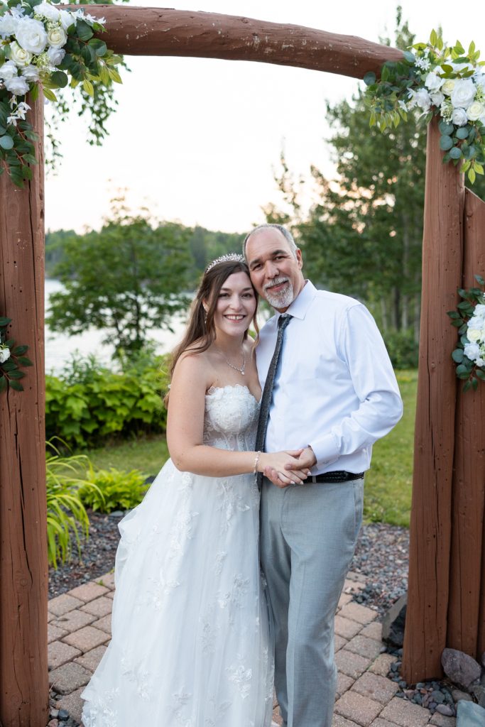 Newly married couple smiling and holding hands beneath a floral archway at their Wisconsin wedding