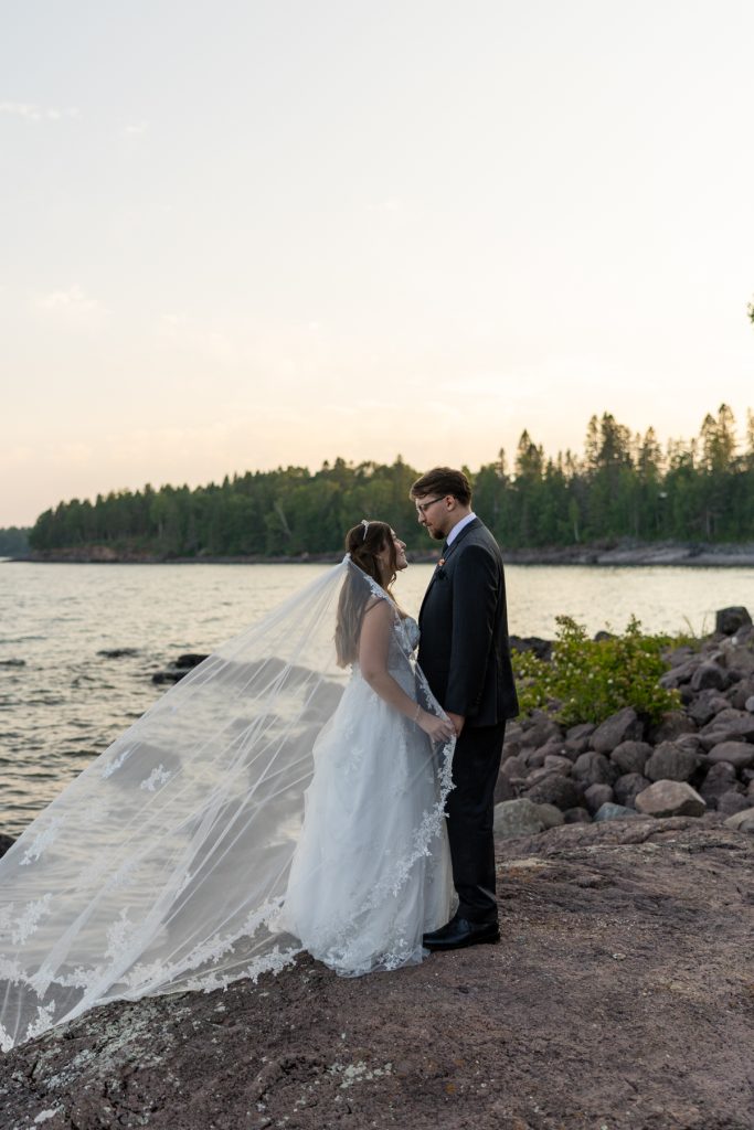 Bride and groom embracing at sunset near a lake, showcasing a romantic wedding photography moment