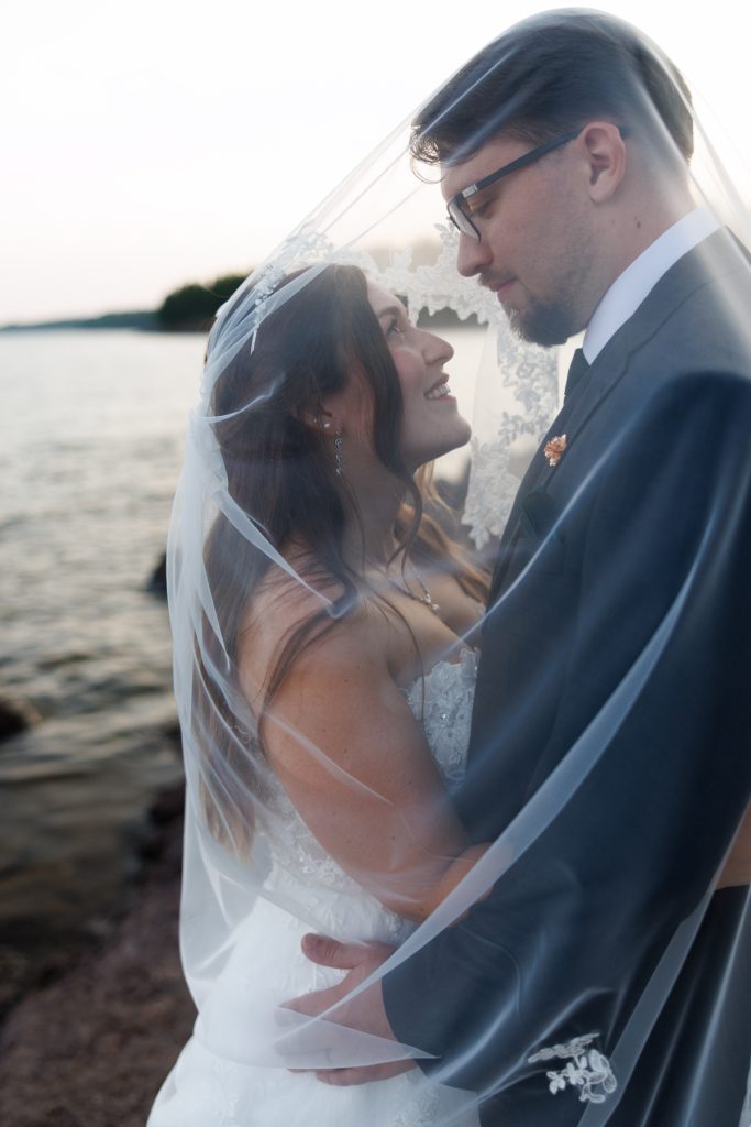 Bride and groom embracing tenderly under a flowing veil during their wedding day