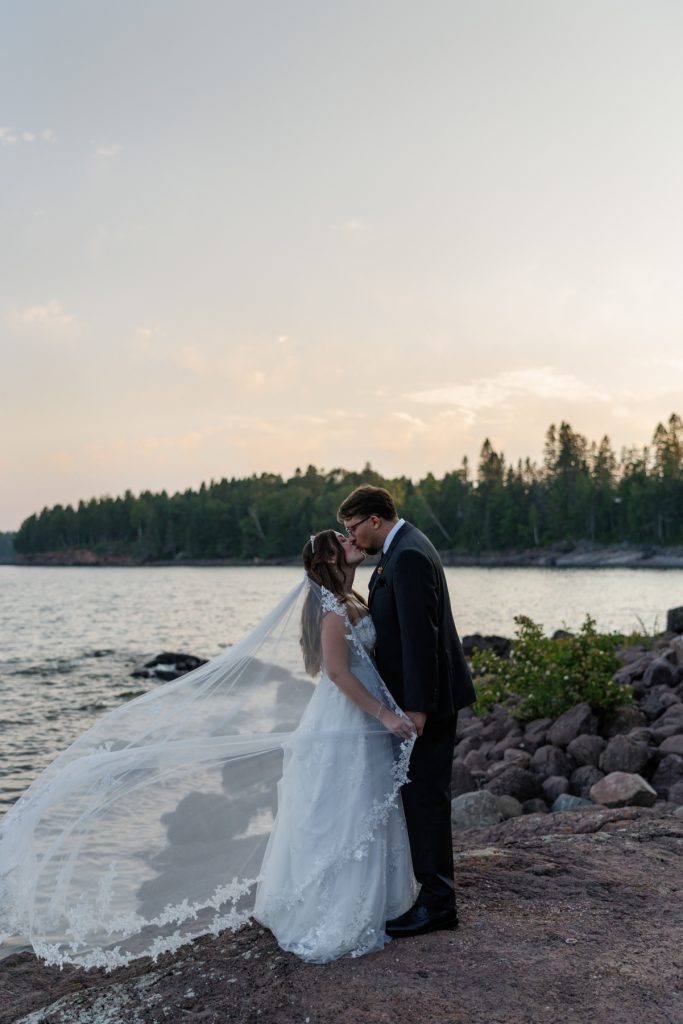 Bride and groom share a romantic kiss during their wedding day near a lake
