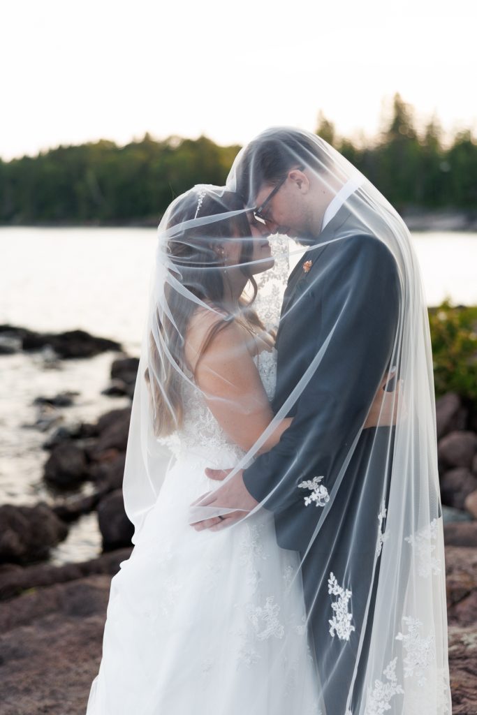 Bride and groom embracing tenderly beneath a flowing veil during a Wisconsin wedding, captured
