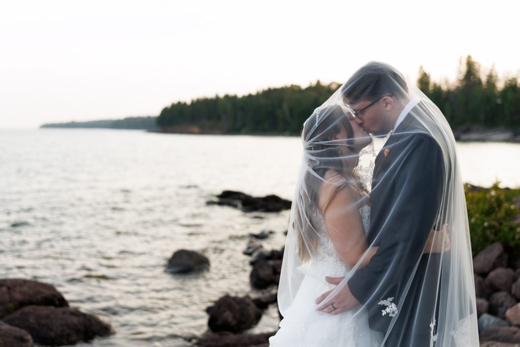 Bride and groom share a romantic kiss enveloped in a flowing veil during a Wisconsin