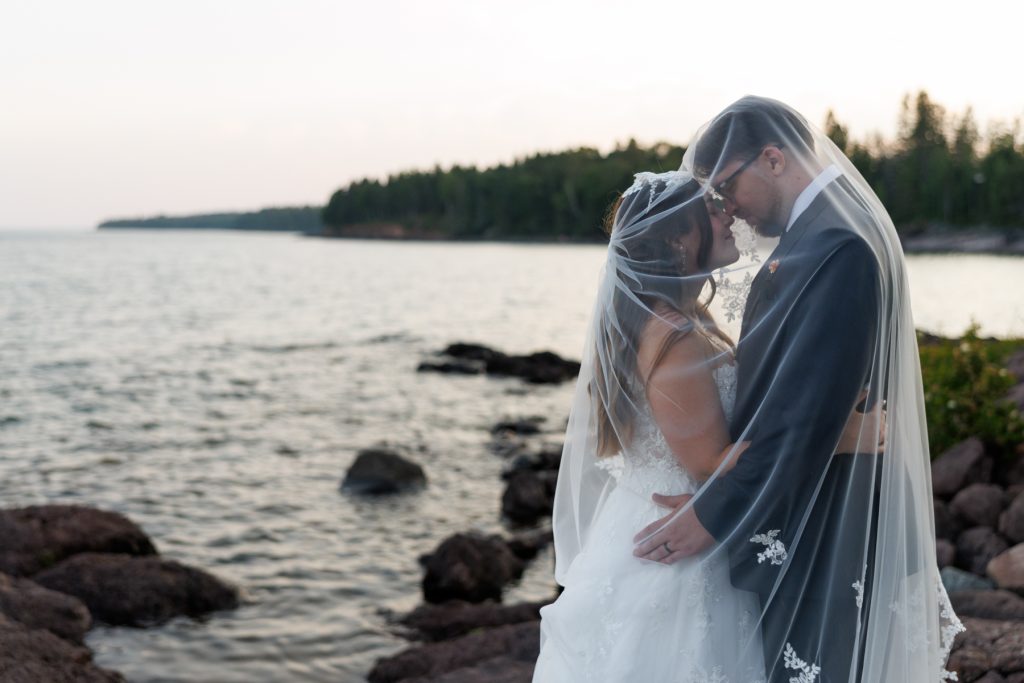 Bride and groom share a romantic moment enveloped in a sheer veil, captured by Beau