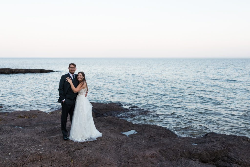 Newly married couple embracing on a rocky shoreline, showcasing Wisconsin and Minnesota wedding photography