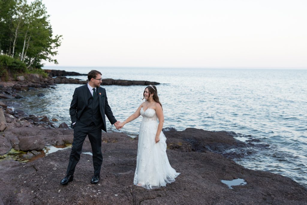 Newly married couple holding hands, smiling, and gazing at the lake during their Wisconsin wedding
