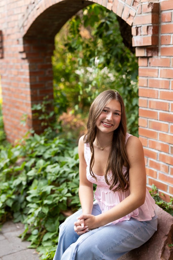 Abby, a Hayward Wisconsin High School senior, smiles warmly while seated near a brick archway