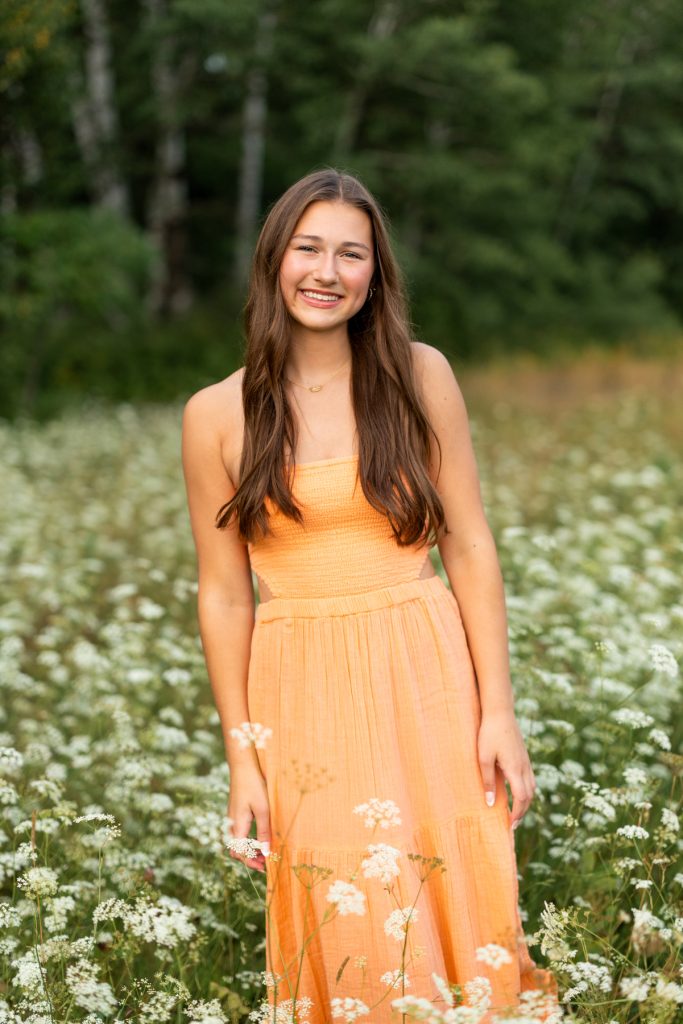 Hayward Wisconsin High School senior Abby smiling in an orange dress surrounded by a field