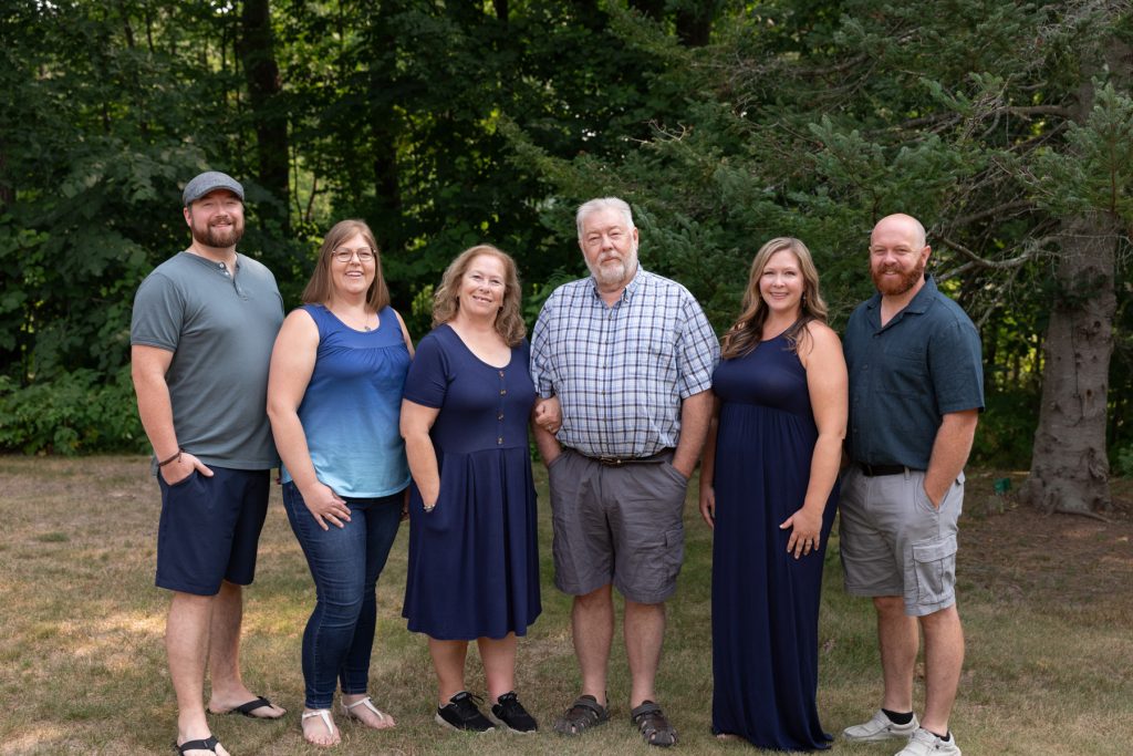 A multigenerational family poses for a portrait session in a wooded area, capturing cherished memories