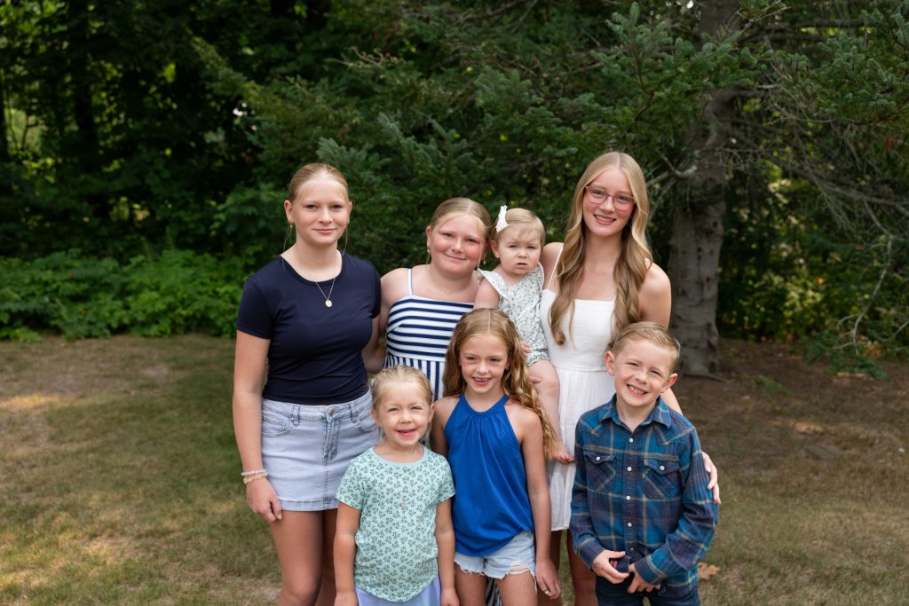 A family portrait showcases four daughters and two sons posing together outdoors, capturing cherished memories