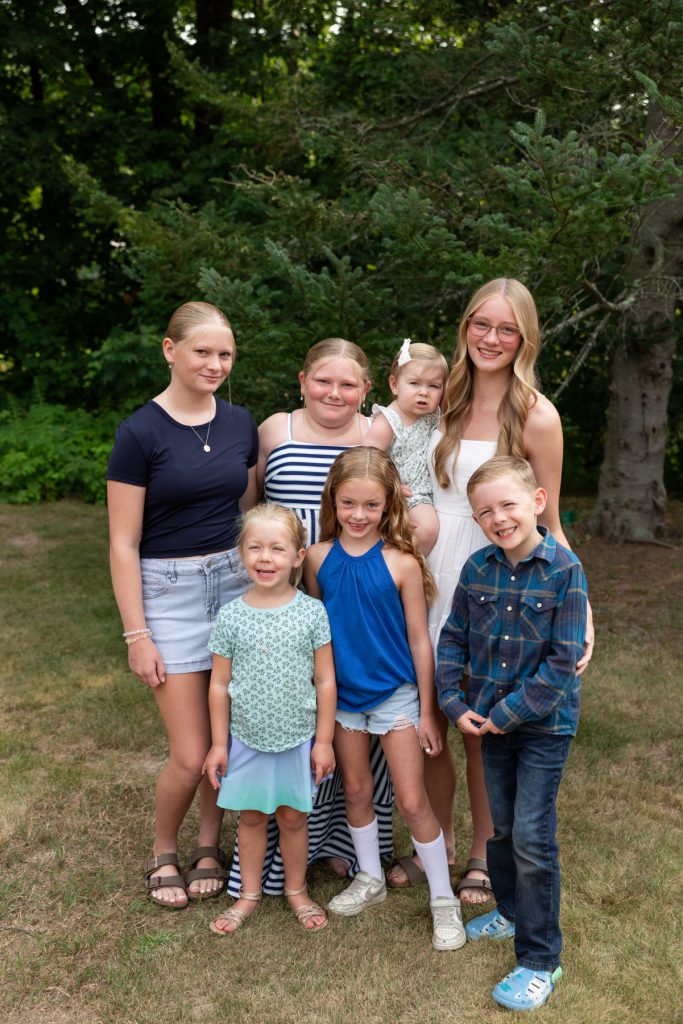 A large family portrait featuring seven children smiling and posing outdoors, showcasing memories captured