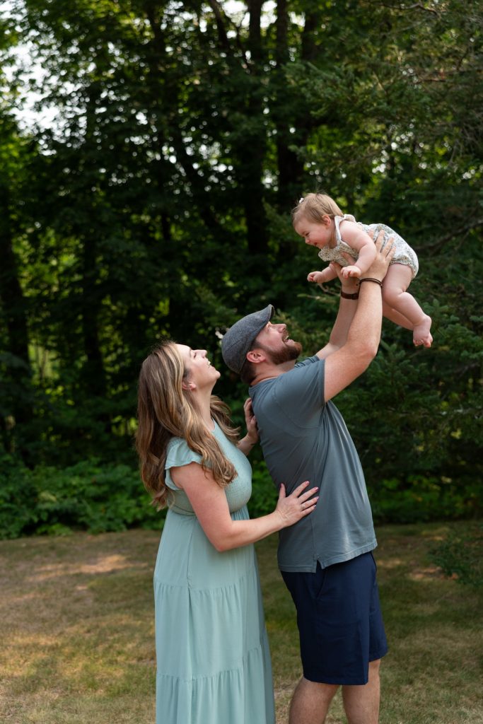 A joyful family portrait captures a couple playfully lifting their baby daughter high