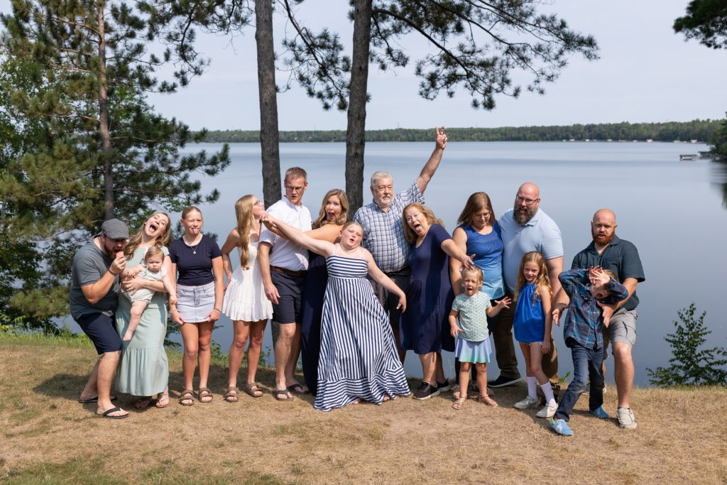 Large multigenerational family group posing playfully for a portrait session near a lake in Wisconsin