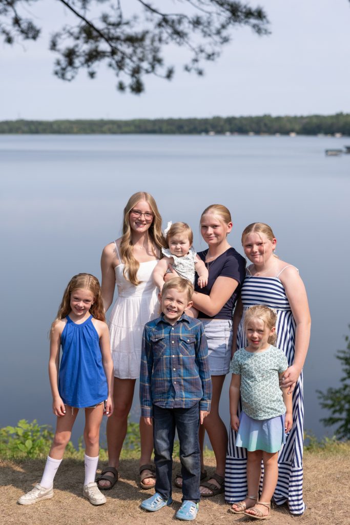 A large family portrait showcases six children and a baby posed by a lake, capturing