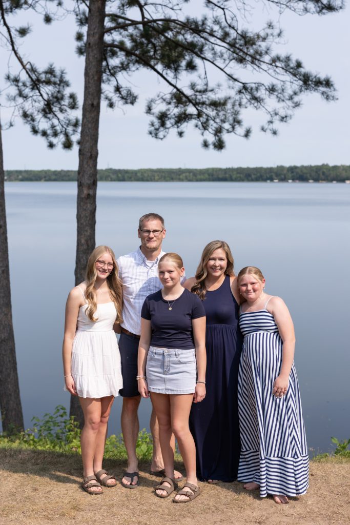 A family portrait session captures a father and four daughters standing near a lake