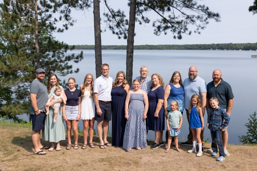 Large multigenerational family poses for a portrait session near a lake, capturing cherished family time