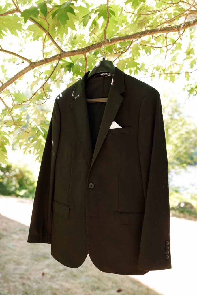 A black suit and white pocket square hanging from a tree branch, showcasing wedding attire