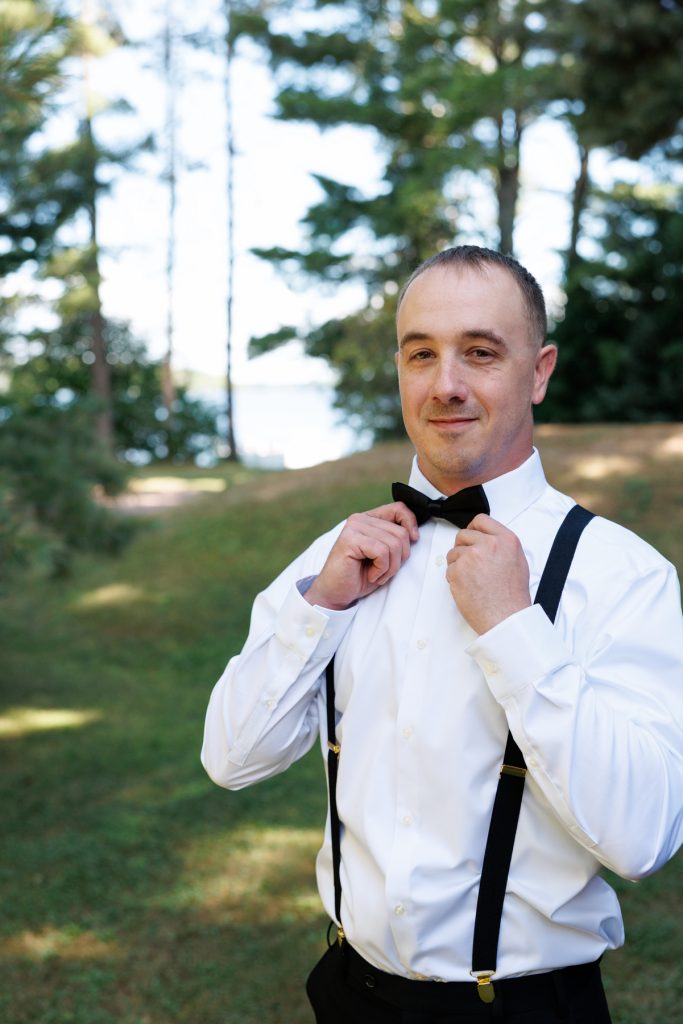 Groom adjusting his bow tie and suspenders at a Lakewoods Resort wedding in Cable, Wisconsin