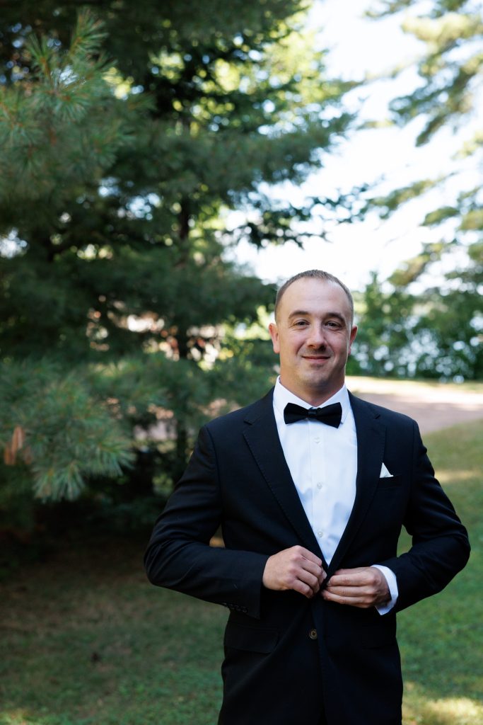 Groom in a black tuxedo and bow tie adjusts his jacket during a Lakewoods Resort