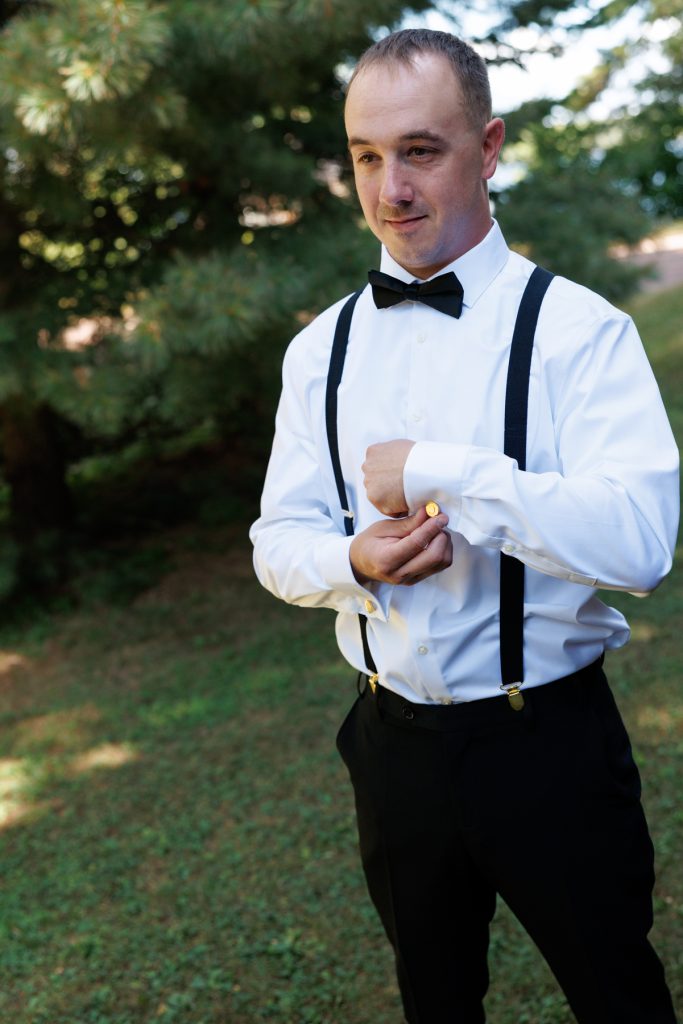 Groom in a white shirt, black bow tie, and suspenders adjusting cufflinks, captured by Beau