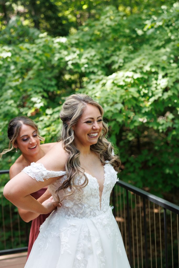 Bride Bianca smiles as her bridesmaid adjusts her detailed wedding gown at Lakewoods Resort