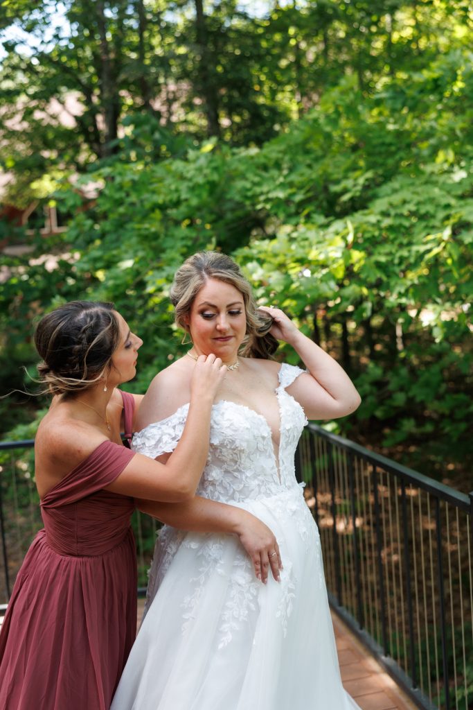 Bride in a white lace wedding dress receiving assistance from a bridesmaid in a burgundy