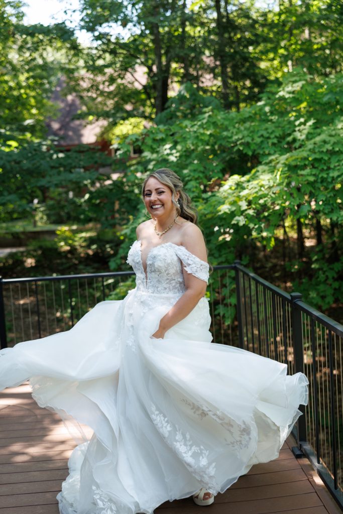 Bride in a flowing wedding dress twirls on a wooden bridge at Lakewoods Resort, captured