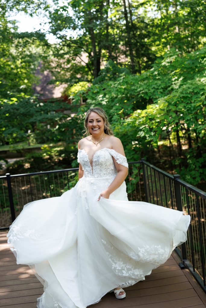 Bride in a flowing off-the-shoulder wedding dress twirls on a wooden deck at Lakewoods Resort