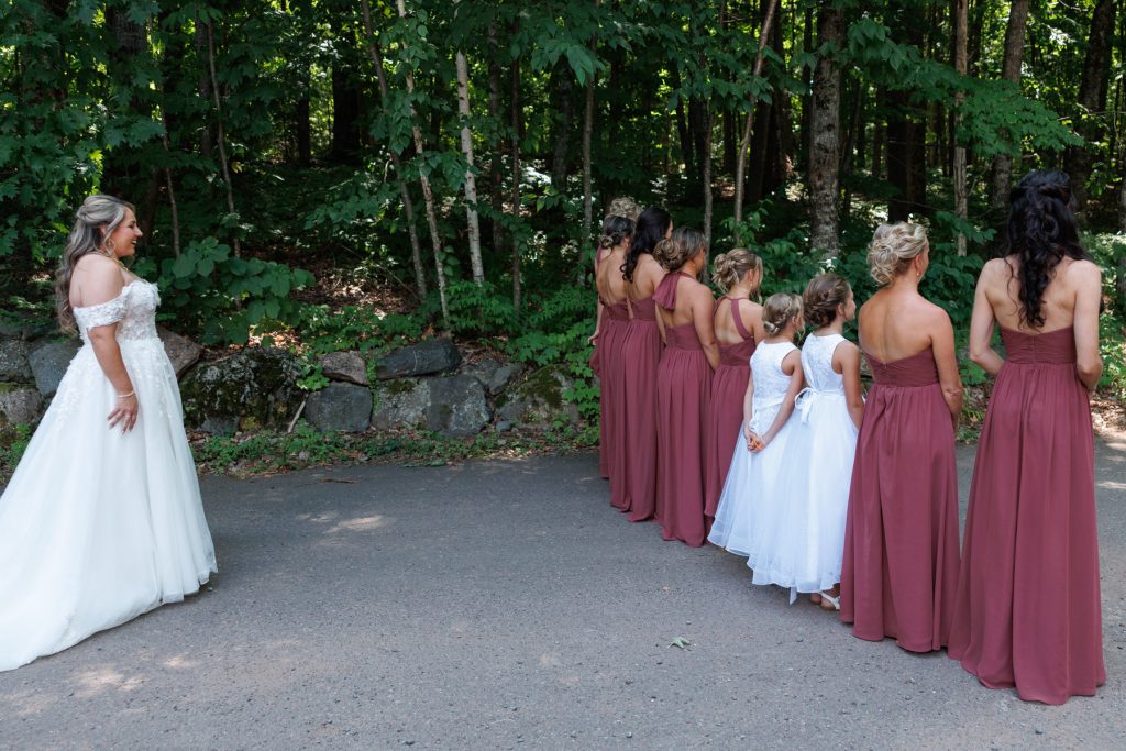 Bride in a white wedding gown facing a line of bridesmaids in maroon dresses