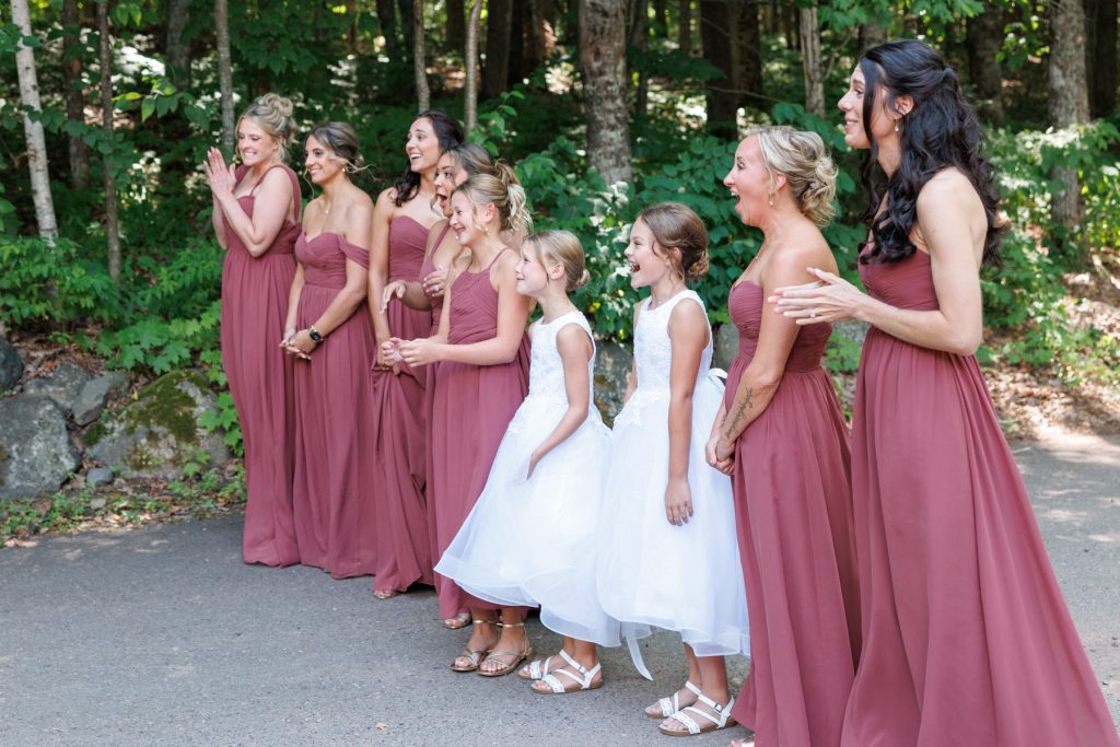 Bride and bridesmaids in matching dresses and flower girls laughing together outdoors at a Lakewoods