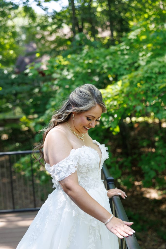 Bride Bianca in a detailed white wedding gown smiles while walking along a wooded path