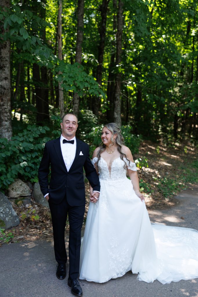 Bianca and Nick, the happy couple, walk hand-in-hand along a wooded path at Lakewoods Resort