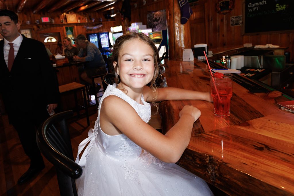 Young girl in a white dress smiles while leaning on a wooden bar