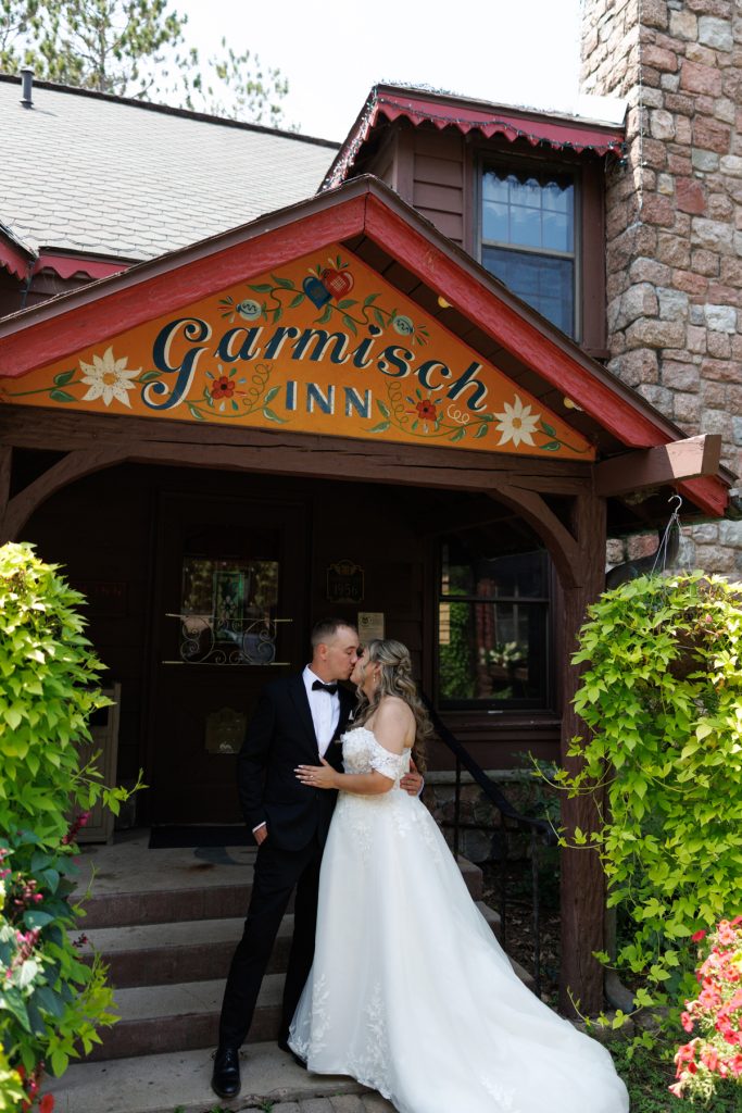 Bride and groom in formal wear share a kiss in front of the Garmisch Inn