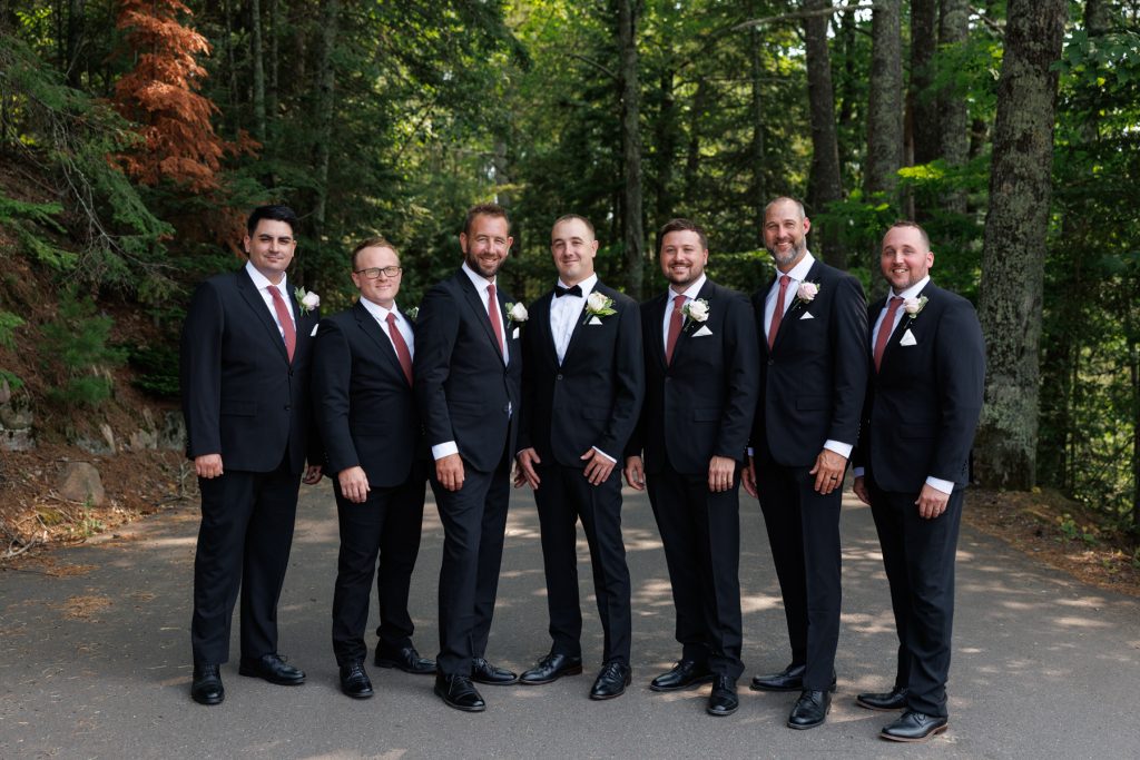 The groom and groomsmen, dressed in suits and bowties, pose for a wedding party photograph