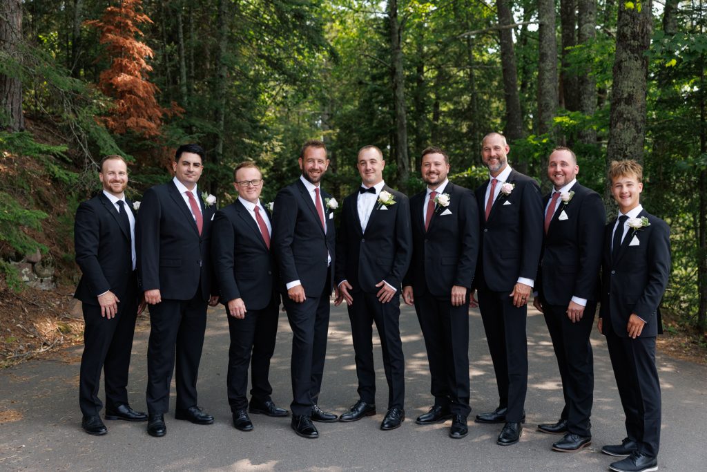 Groom and groomsmen in black suits and red ties pose for a wedding photograph