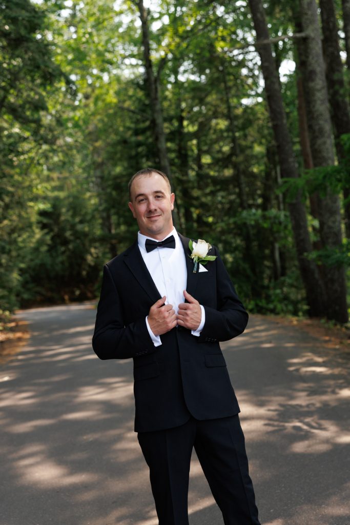 Groom in a classic tuxedo and floral boutonniere smiles for a portrait during a Lakewoods