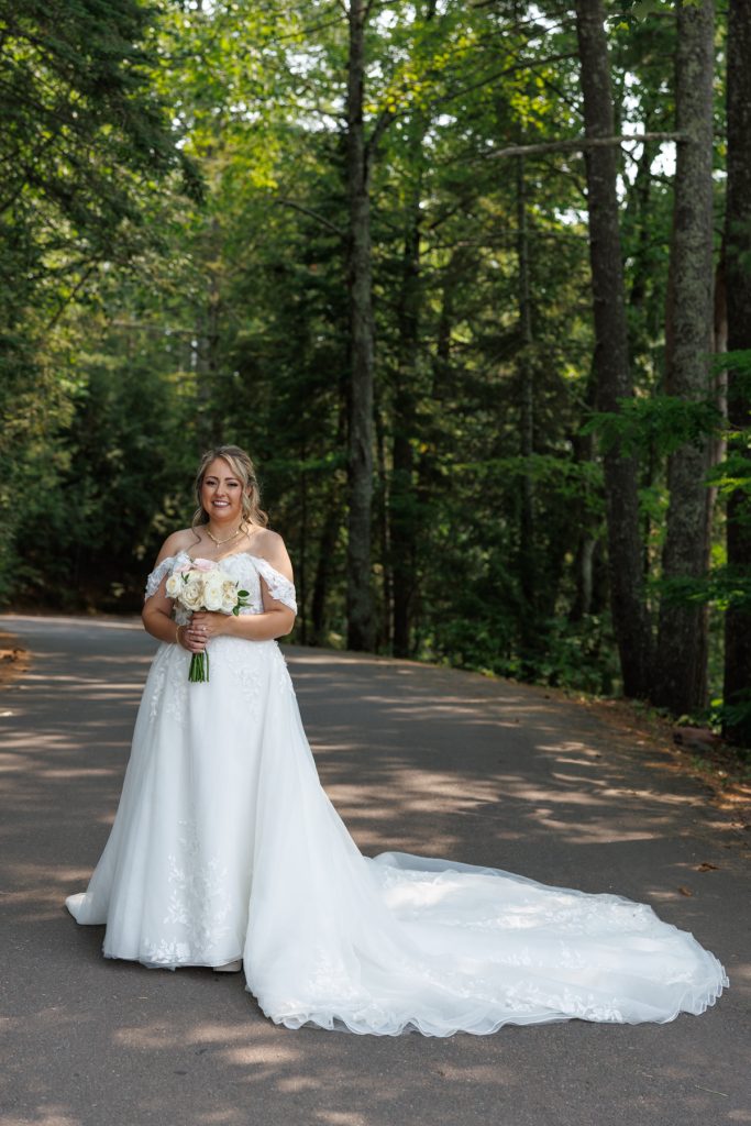 Bride in a flowing white gown stands on a lakeside road at a Lakewoods Resort