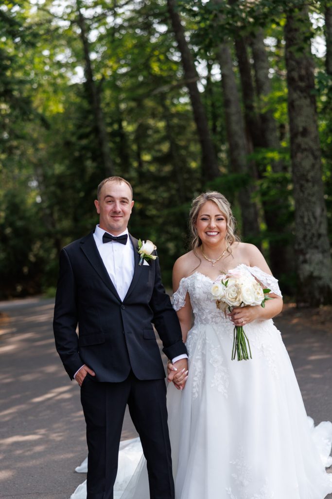 Bianca and Nick, the newlyweds, pose together in formal wedding attire amidst a lush, wooded