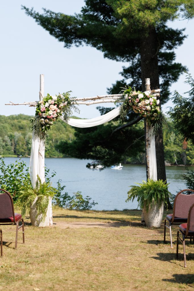 Elaborate floral archway decorated with greenery and flowing fabric overlooking Lake Namekagon at a Lakewoods