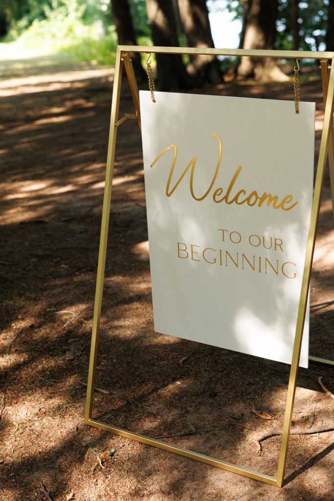 Elegant gold-framed welcome sign reading "Welcome to Our Beginning" displayed outdoors at Bianca and Nick’s