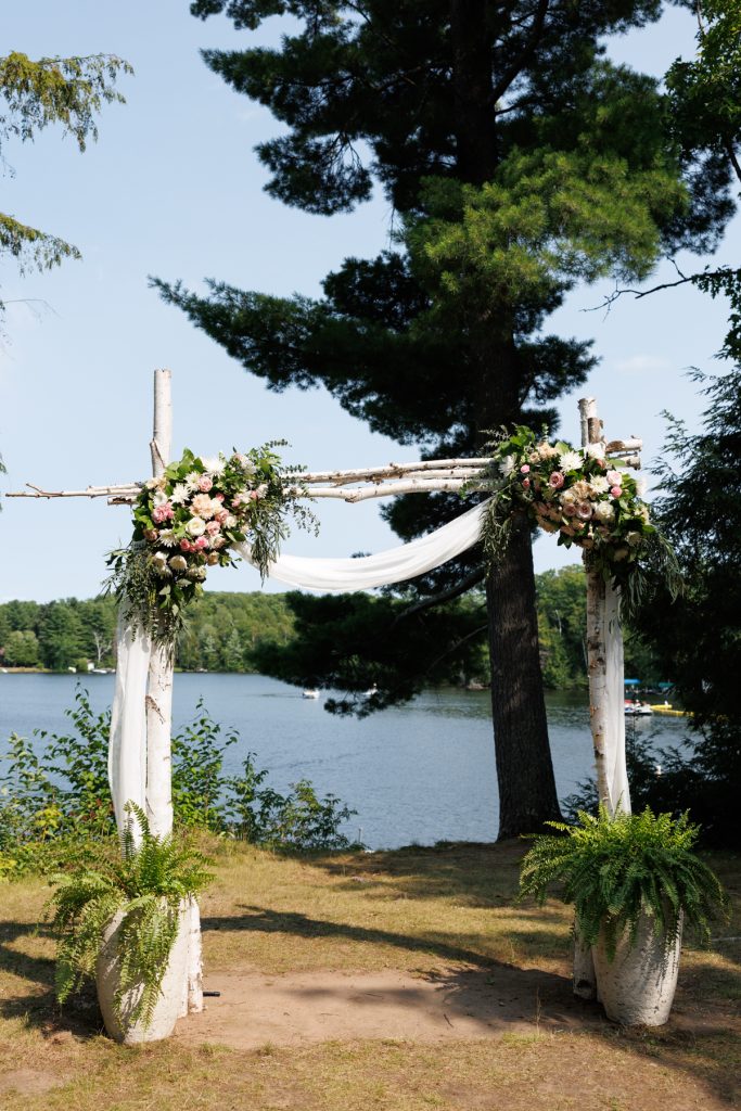 Elaborate floral archway decorated with flowing fabric, set against a lake backdrop at a Lakewoods