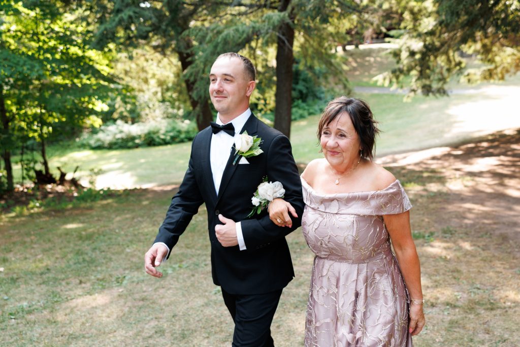 Groom in tuxedo walks arm-in-arm with his mother at Lakewoods Resort wedding in Cable, Wisconsin